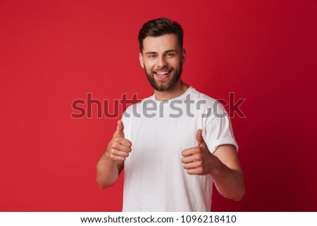Picture of happy young handsome man standing isolated over red wall background. Looking camera showing thumbs up.