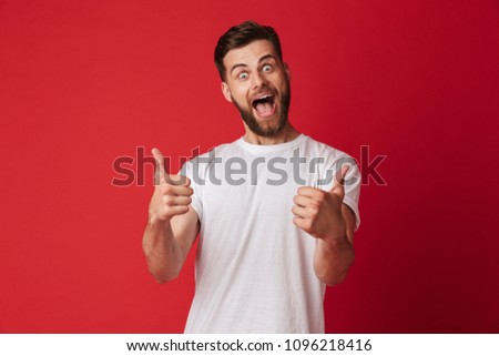 Picture of happy young handsome man standing isolated over red wall background. Looking camera showing thumbs up.