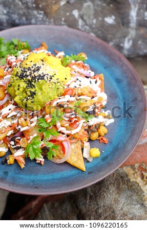 Yellow corn nacho chips garnished with ground beef, guacamole, melted cheese, peppers