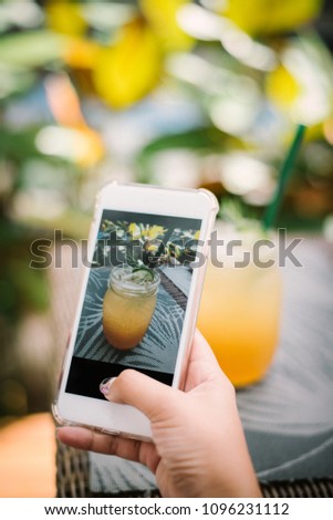 Teenage girl's hands with smartphone takes picture of lemon tea on table for social networks post in the garden