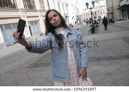 Attractive girl make selfie on city street.
