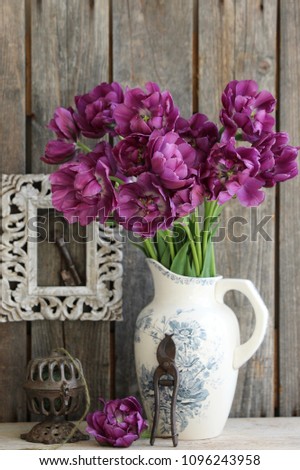 Floral composition with tulips in old antique, vintage faience pitcher, rustic key in aged frame, string twine holder, garden scissors on dark wooden weathered background, vertical photo, daylight 