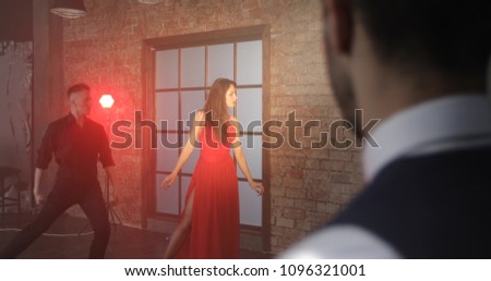 A rich man is jealous of a woman in a red dress dancing tango with a dancer.  Retro studio.