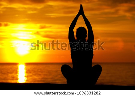 Silhouette of yoga woman raising hands and meditating against sea background on warm sunny day during sunset