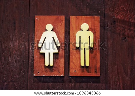 Wood signboard in front of the toilet. Divide between men and women.
