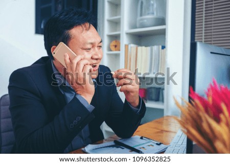 Businessman in suit talking on phone working on computer, busy entrepreneur making answering call sitting at office desk with computer, speaking to client by cell, using gadgets for business