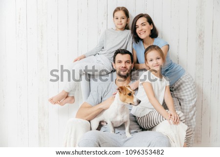 Family portrait. Happy parents with their two daughters and dog pose together against white background, spend free time at home, being in good mood. Mother, father and small sisters pose indoor Royalty-Free Stock Photo #1096353482