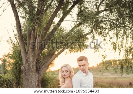 Portraits of young bride and groom walking on the sunset background. Newlyweds on a summer field with sun rays. 
