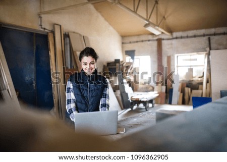 Portrait of a woman worker with laptop in the carpentry workshop.