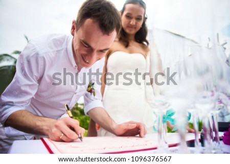 The groom signs documents on registration of marriage and smiles. A young couple signs the wedding documents. Outdoor wedding ceremony