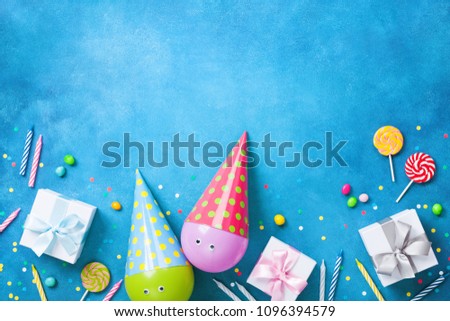 Holiday background with funny balloons in caps, gifts, confetti, candy and candles. Flat lay. Birthday or party greeting card with copy space.