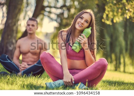Healthy lifestyle concept. Happy young fitness couple sitting in lotus pose on a green grass.