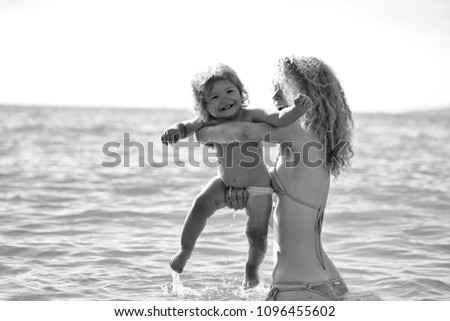 Kids enyoj happy day. Young mother in bikini standing swimming and playing with male child boy in sea or ocean water sunny day outdoor on natural background, horizontal picture
