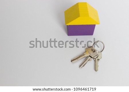 Three metal keys and a purple toy house with a yellow roof on a white background