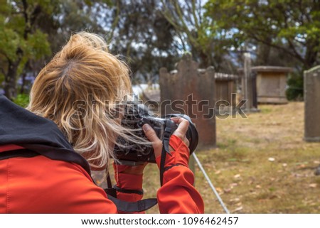 Travel photographer woman holding her camera up to take a photo in an ancient cemetery a Port Arthurt in the Island of the Dead, Tasmania, Australia.