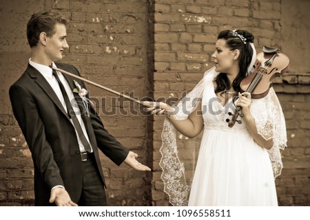 The bride is having fun with the groom playing with the violin,a black and white photo