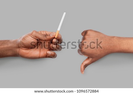 African-american man showing cigarette and thumb down gesture on gray background. Bad addiction and healthy lifestyle concept. No smoking