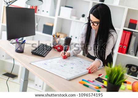 A young girl in glasses stands near the table, holds a marker in her hand and draws on a magnetic board.