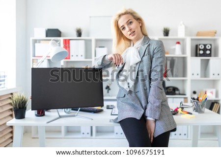 Young girl stands in office, leaning on desk. Nearby is a monitor.