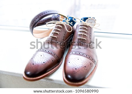 Men's new leather brown shoes closeup still life isolated with blue polka dot socks, watch, shoelaces laces tied, wedding or interview preparation, belt on windowsill in room