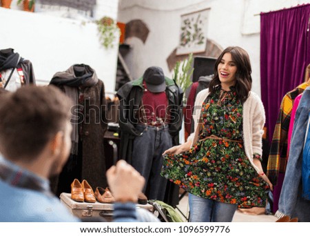 sale, shopping, fashion and people concept - happy young woman posing for boyfriend at vintage clothing store
