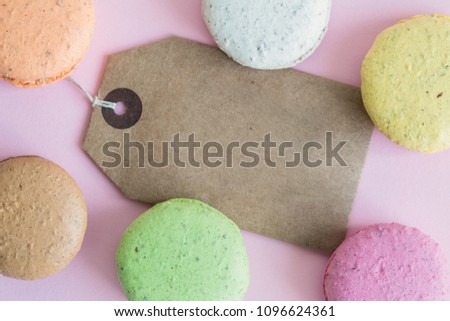Flat lay of colorful macaroons and blank price tag against pastel pink background.