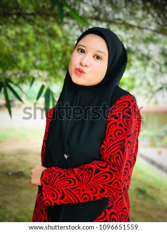 Portrait of beautiful young Asian Muslim woman wearing Baju Kurung and hijab posed under a bamboo tree. 