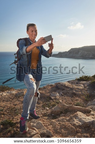 Full length portrait of smiling girl with backpack making selfie against the ocean