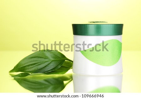 Jar of cream with green leaves on green background