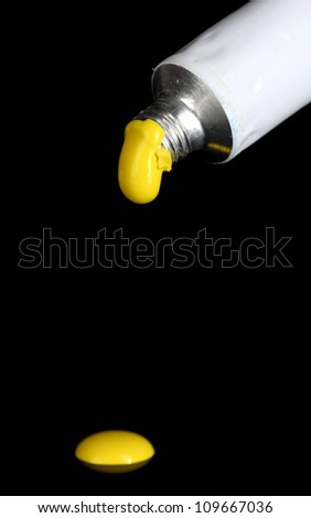Yellow paint follows from the tube on black background close-up