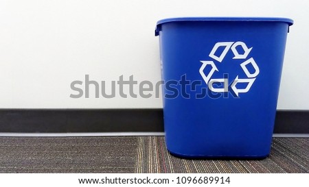 A blue recycle bin sits on the floor of an office.