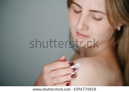 Attractive beautiful woman applying moisturizer cream on her body after shower. Photo of young girl with flawless skin isolated on gray background. Cosmetology. Close up. Skin care and beauty concept.