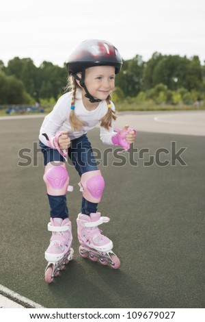 portrait of small little caucasian blond girl skating outside on stadium track in protective helmet