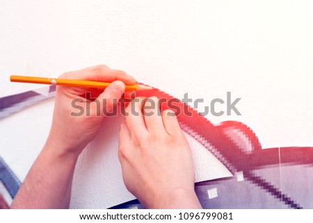Close up a young dark-haired woman in a plaid shirt draws a large red car in the boy's room on the wall. Mom paints his son car, he traces the contour of a law-book with a pencil