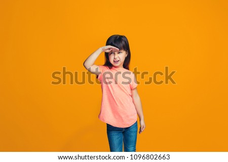Happy teen girl standing, smiling and looking away isolated on trendy orange studio background. Beautiful female half-length portrait. Human emotions, facial expression concept.