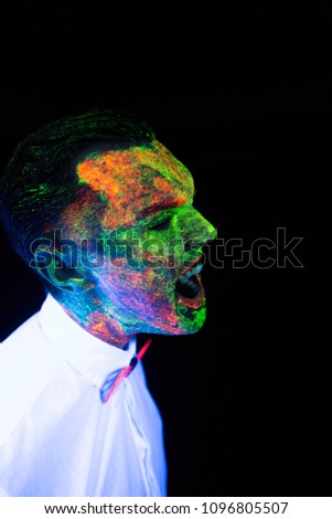 concept of wedding photosession in neon lighting in vogue style groom young guy screams ana roars glows in the dark posing in white wedding suit with a bow tie under the UV rays on a dark background