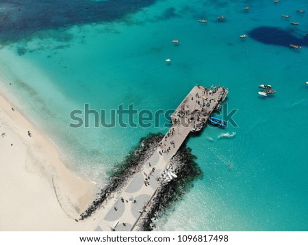 Aerial photo of the beautiful pier and beach at Cape Verde showing boats with fishermen and fishermen's wives on the pier selling fish from the daily catch, the sea is clear and blue.