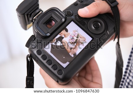 Professional photographer holding camera with lovely wedding couple on display, closeup Royalty-Free Stock Photo #1096847630