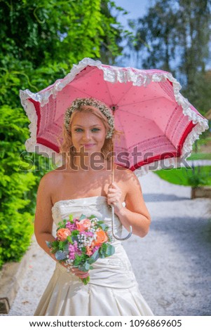A young bride isholding a nice colourful bouquet in her hand. In the other hand, she is carrying an umbrella.