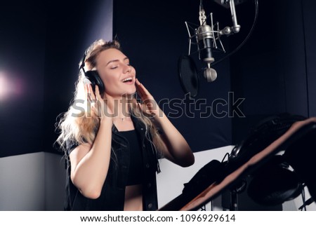 Wonderful voice! Pretty smiling graceful young singer woman focused on recording her new hit in the modern studio in front of the microphone.