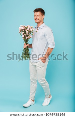 Image of young caucasian man isolated over blue background holding flowers.