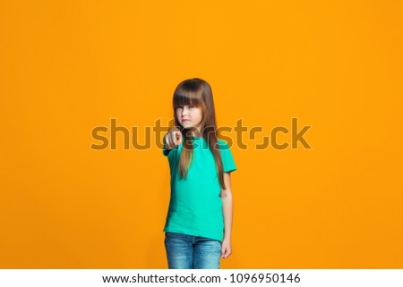 I choose you and order. The smiling teen girl pointing to camera, half length closeup portrait on orange studio background. The human emotions, facial expression concept. Front view. Trendy colors