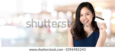 Young smiling beautiful Asian woman presenting credit card in hand, showing trust and confidence for making payment, on panoramic banner bokeh  background with copy space