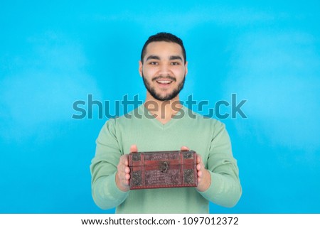 Young man wearing a casual outfit, holding a jewelry box and giving it to someone,  standing on a blue background