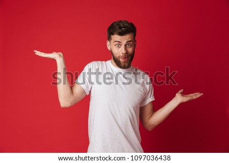 Picture of emotional young handsome man standing isolated over red wall background. Looking camera showing copyspace.