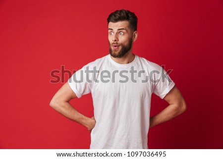 Picture of excited young handsome man standing isolated over red wall background. Looking aside.