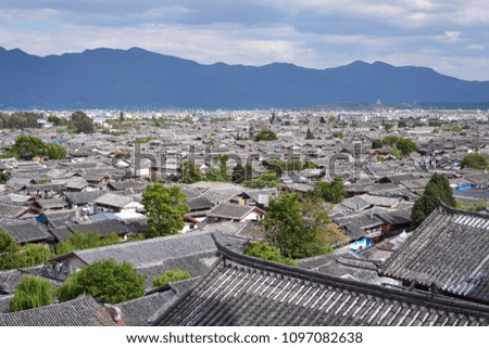 Bird's-eye view of many ancient chinese house and trees at Lijiang old town in China with mountain in background. It famous view for take photo of traditional roofs.