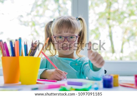 Little girl drawing paints and crayons to a room with a window. Cute child doing homework. Creative kid. Girl showing OK sign.