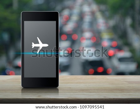 Airplane icon on modern smart phone screen on wooden table over blur of rush hour with cars and road, Business transportation concept