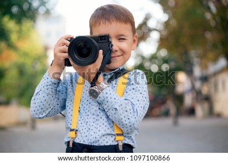 Boy, in blue shirt, silver watch and yellow suspenders, makes pictures on film retro style digital camera, stylishly dressed, photographer, outdoor portrait, close up, street photo.